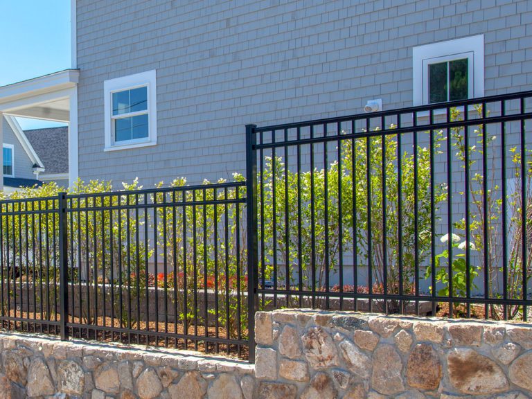 closeup view of black aluminum fence and plantings in front of a shingled building