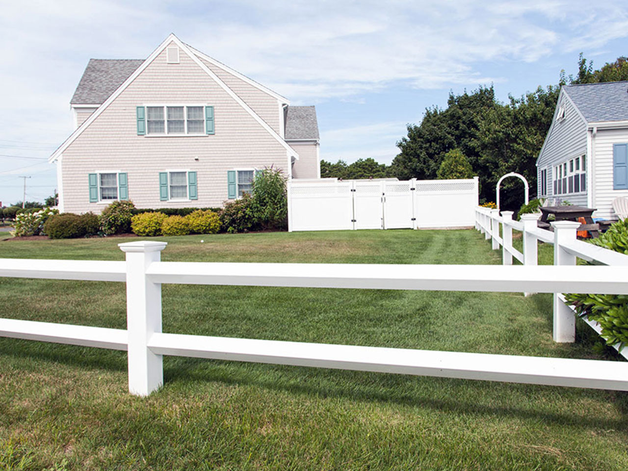 white post and rail fence around the yard of a summer home and nice green lawn