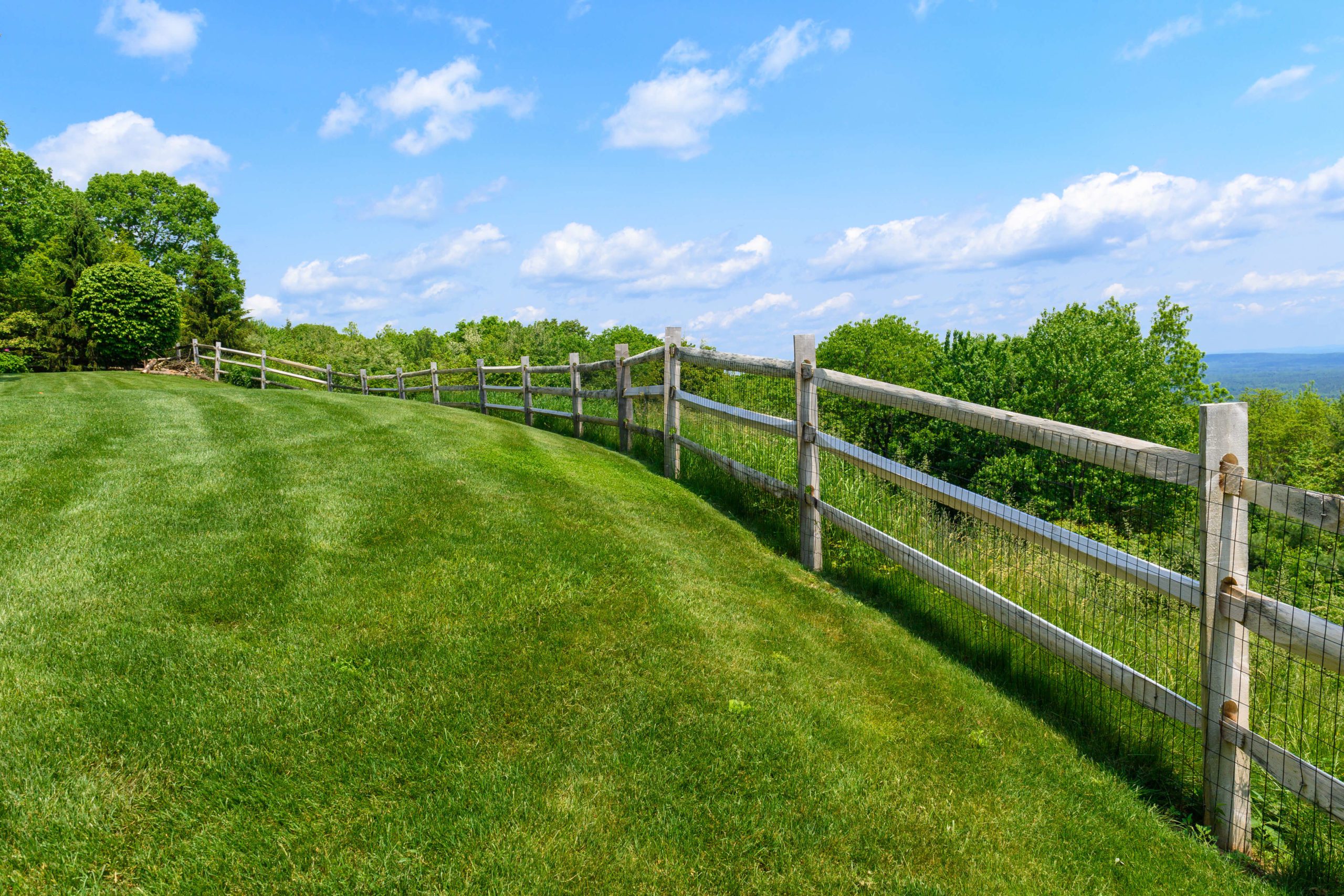 wooden post and rail fence with wire on a lush green lawn overlooking a valley
