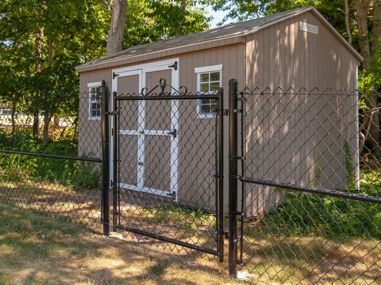 black chain link fence in front of a tan garden shed set in the woods